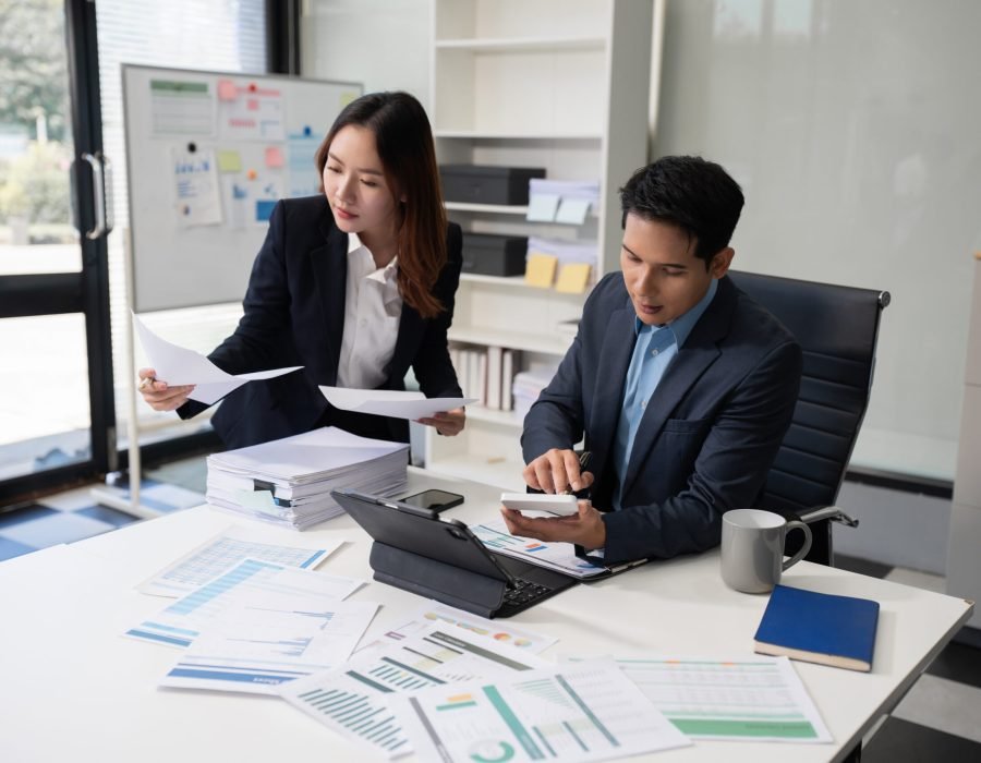 Business team analyzing documents, graphs, and data with a laptop, tablet, and smartphone. Collaboration, strategy, and success in a modern office.