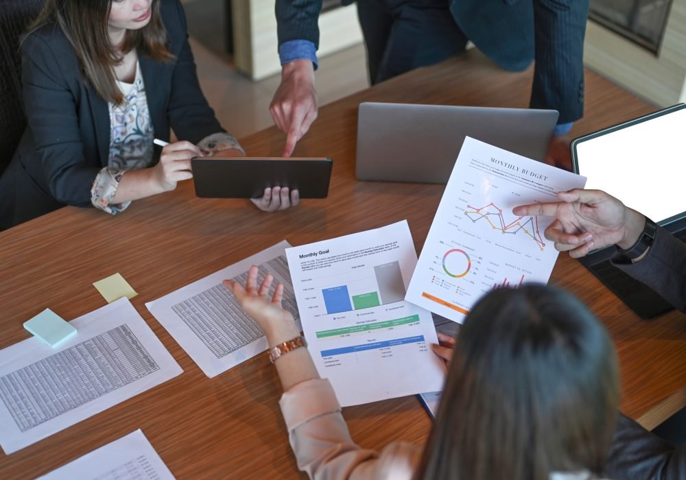 Executive businesspeople brainstorming and analyzing financial reports together in meeting room.
